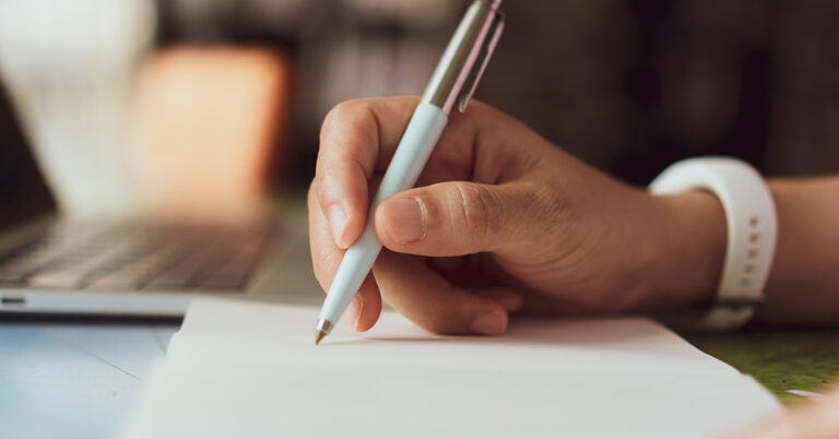 Nahaufnahme einer Hand, die einen Stift hält und beginnt, auf ein weißes Blatt Papier zu schreiben. "Getting things done" ist eine bewährte Strategie, um Struktur in den (Berus-)Alltag zu bringen.