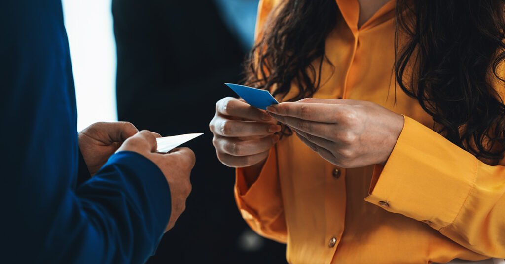 Zwei Personen stehen sich gegenüber und halten je eine Visitenkarte in den Händen. In solchen Situationen können durchaus auch Networking-Fehler auftreten.