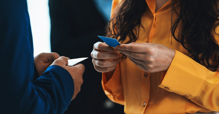 Zwei Personen stehen sich gegenüber und halten je eine Visitenkarte in den Händen. In solchen Situationen können durchaus auch Networking-Fehler auftreten.