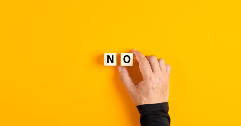 Symbolbild zum Thema Nein sagen: leuchtend gelber Hintergrund, darauf legt eine männliche Hand zwei Würfel mit den Buchstaben N und O ab