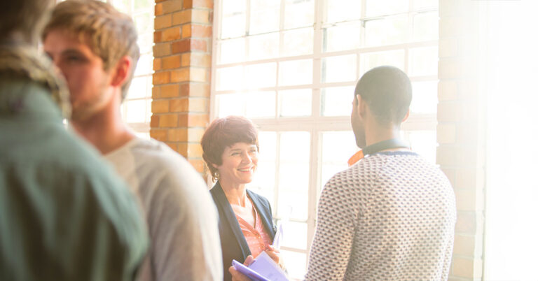 Frau und Mann unterhalten sich in Loft vor einem großen Fenster, daneben weitere Personen. freundliche, positive Atmosphäre