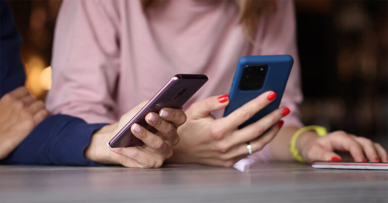 digitale Ablenkung: zwei Frauen sitzen nebeneinander und halten Smartphones mit farbigen Hüllen in den Händen