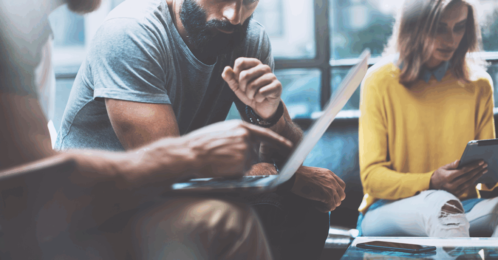 drei Kollegen sitzen nebeneinander, zwei davon schauen gemeinsam auf einen Laptop und reden Kalrtext über ein Projekt