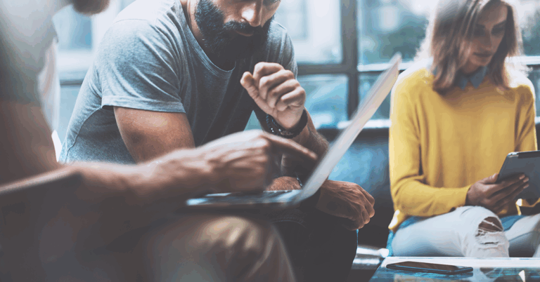 drei Kollegen sitzen nebeneinander, zwei davon schauen gemeinsam auf einen Laptop und reden Kalrtext über ein Projekt
