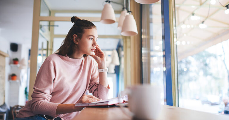 Was wäre wenn: Junge Frau sitzt nachdenklich an einem Tisch