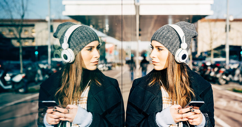 eine junge Frau lehnt an einer Scheibe und betrachtet ihr Spiegelbild. Symbolbild zum Thema Selbstreflexion.