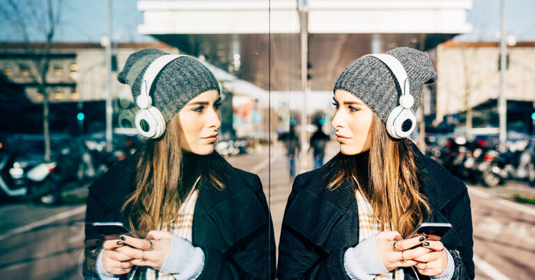 eine junge Frau lehnt an einer Scheibe und betrachtet ihr Spiegelbild. Symbolbild zum Thema Selbstreflexion.